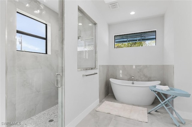 bathroom with independent shower and bath, a healthy amount of sunlight, and tile walls