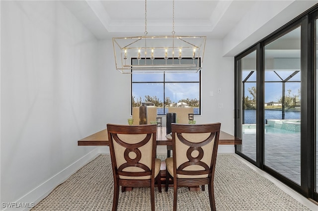 dining space featuring a raised ceiling, a notable chandelier, a water view, and carpet floors