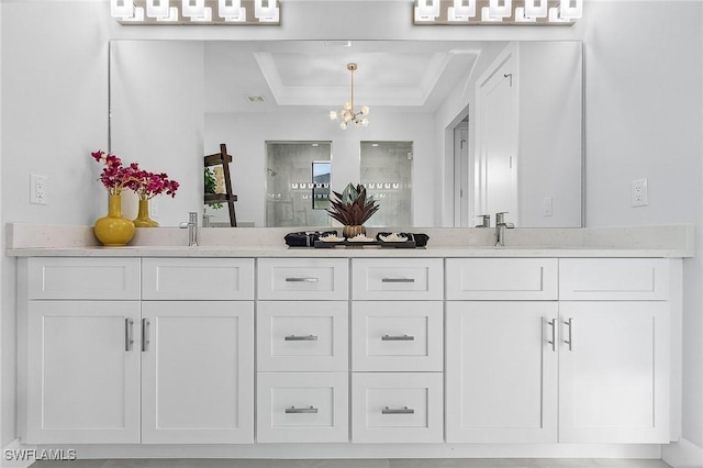 bathroom with a tray ceiling, vanity, a chandelier, and walk in shower