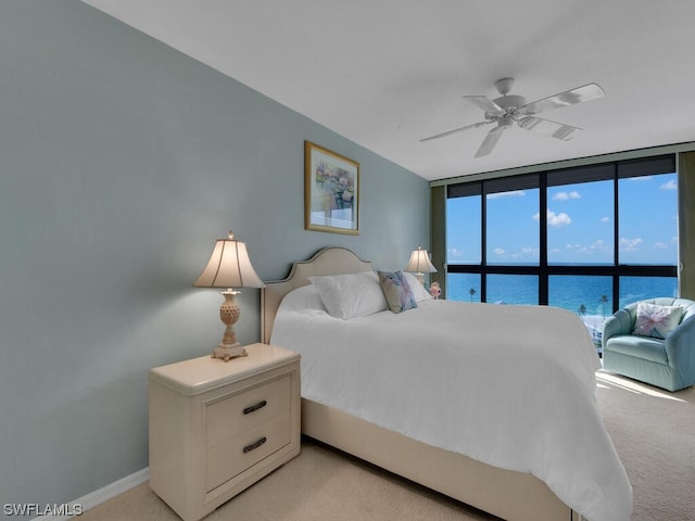 bedroom featuring a water view, floor to ceiling windows, ceiling fan, and light colored carpet