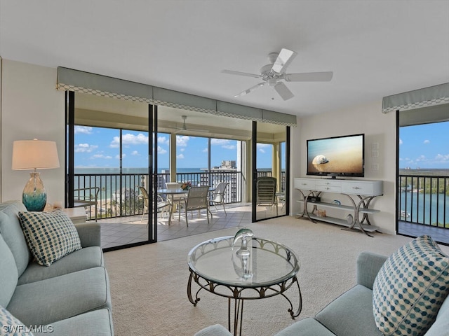 living room featuring light colored carpet, ceiling fan, and a water view