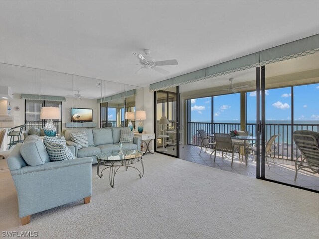 living room with plenty of natural light, a water view, light colored carpet, and ceiling fan