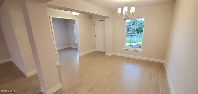 unfurnished room with an inviting chandelier and light hardwood / wood-style flooring