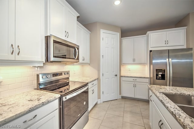 kitchen with white cabinets, backsplash, light tile floors, and stainless steel appliances