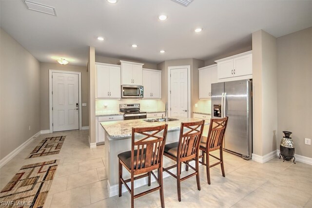 kitchen with sink, a kitchen breakfast bar, white cabinets, a center island with sink, and stainless steel appliances