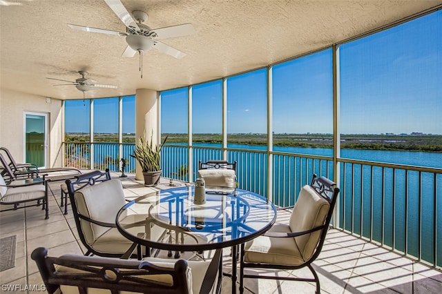 unfurnished sunroom featuring ceiling fan and a water view