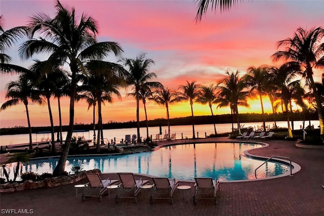 pool at dusk featuring a patio area and a water view