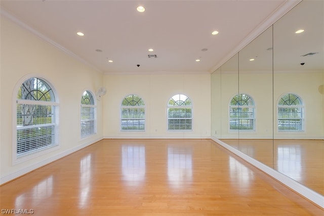 spare room with crown molding, a healthy amount of sunlight, and light wood-type flooring