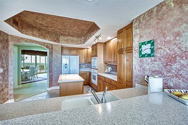 kitchen with kitchen peninsula, white appliances, sink, a tray ceiling, and a textured ceiling