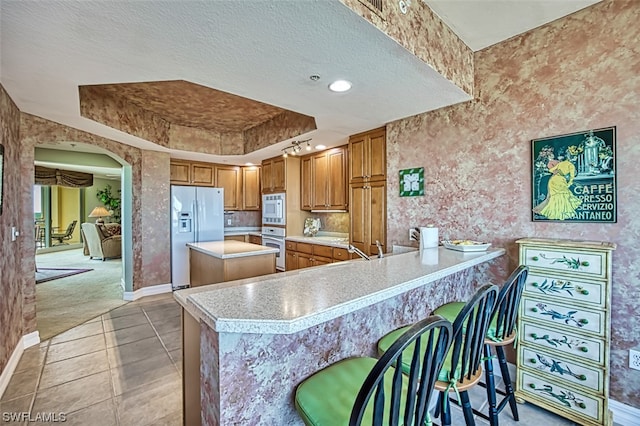 interior space featuring a kitchen breakfast bar, stainless steel appliances, light carpet, a textured ceiling, and a center island