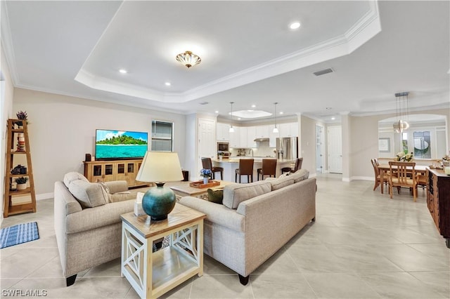 living room featuring light tile patterned flooring, crown molding, and a tray ceiling