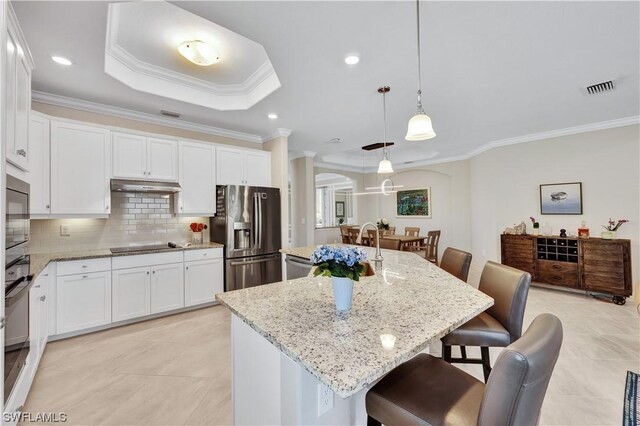 kitchen with a breakfast bar, black appliances, a center island with sink, ornamental molding, and decorative light fixtures