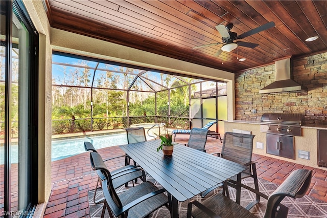 view of patio featuring area for grilling, ceiling fan, exterior kitchen, and glass enclosure