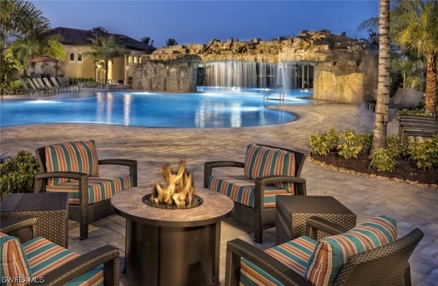 pool at dusk featuring pool water feature, a patio area, and an outdoor fire pit