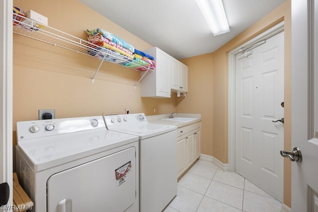 clothes washing area with sink, light tile patterned floors, cabinets, and washer and dryer