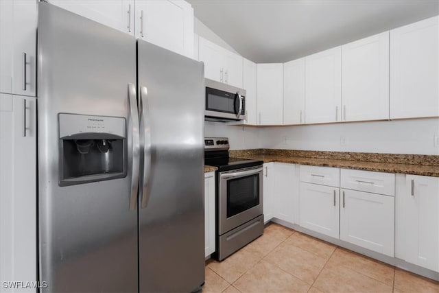 kitchen with lofted ceiling, dark stone countertops, white cabinetry, and stainless steel appliances