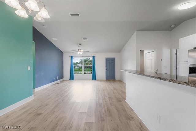 unfurnished living room featuring ceiling fan with notable chandelier, light hardwood / wood-style floors, and lofted ceiling