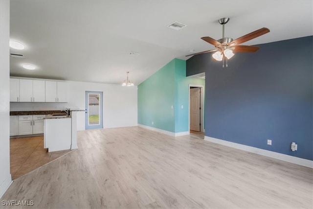 unfurnished living room featuring ceiling fan with notable chandelier, light hardwood / wood-style floors, sink, and vaulted ceiling