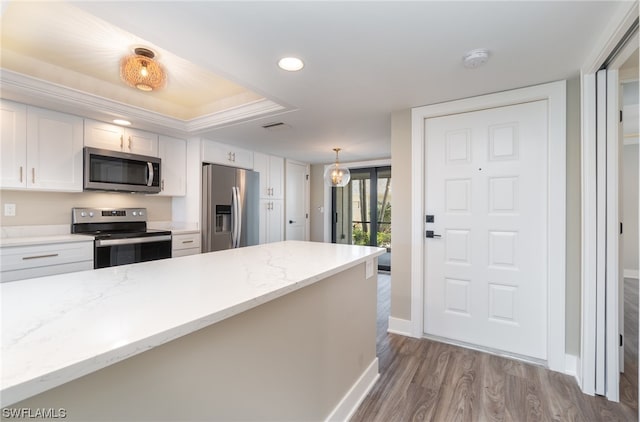 kitchen with light stone countertops, appliances with stainless steel finishes, white cabinetry, hanging light fixtures, and light wood-type flooring