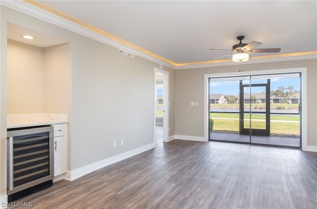 unfurnished living room featuring ceiling fan, beverage cooler, bar, dark wood-type flooring, and crown molding