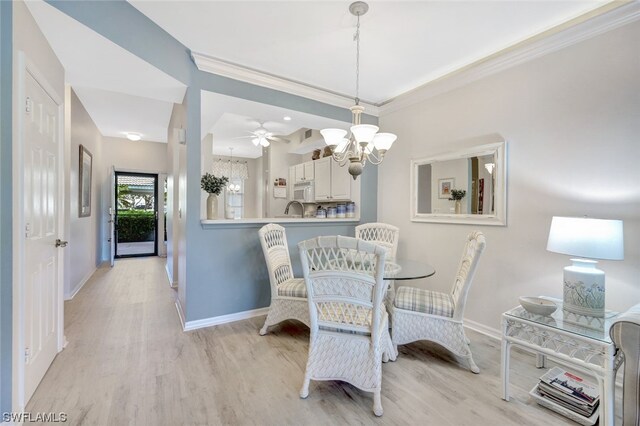 dining space with crown molding, ceiling fan with notable chandelier, sink, and light wood-type flooring