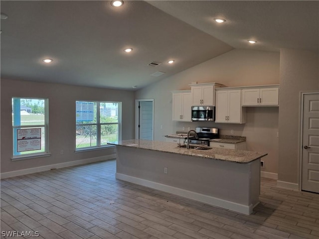 kitchen with white cabinets, appliances with stainless steel finishes, light stone countertops, and an island with sink