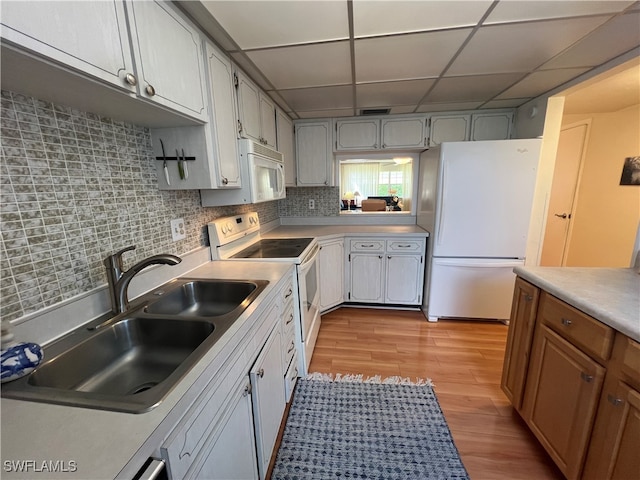 kitchen featuring a drop ceiling, light hardwood / wood-style floors, decorative backsplash, sink, and white appliances