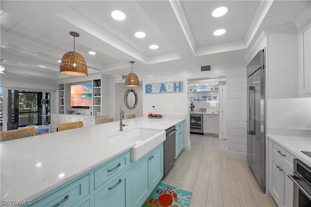 kitchen with sink, hanging light fixtures, stainless steel appliances, light stone countertops, and white cabinetry