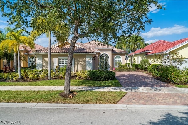 mediterranean / spanish-style home with a tiled roof, decorative driveway, and stucco siding