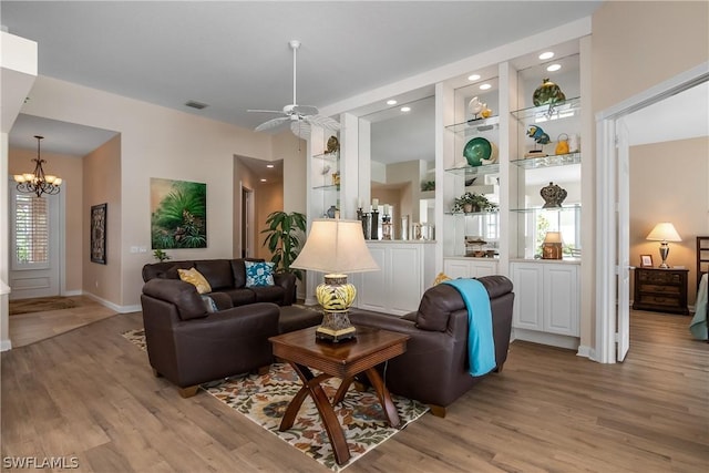 living room featuring built in shelves, a healthy amount of sunlight, ceiling fan with notable chandelier, and light hardwood / wood-style flooring