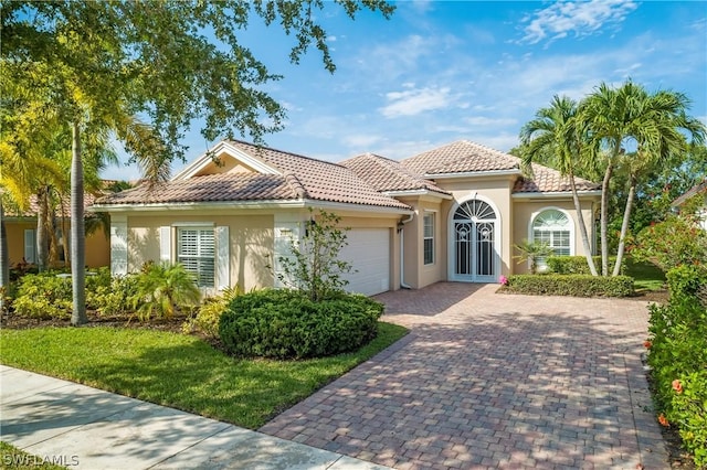 mediterranean / spanish home featuring a garage, decorative driveway, a tile roof, and stucco siding