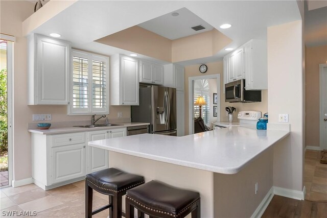 kitchen featuring appliances with stainless steel finishes, a peninsula, light countertops, a kitchen bar, and a sink