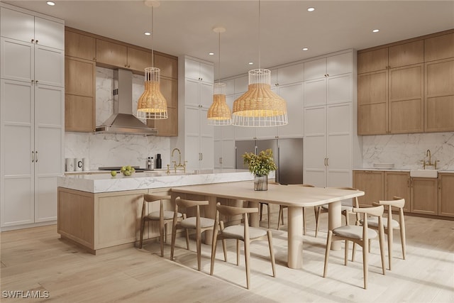 kitchen featuring light wood-type flooring, hanging light fixtures, wall chimney range hood, and sink