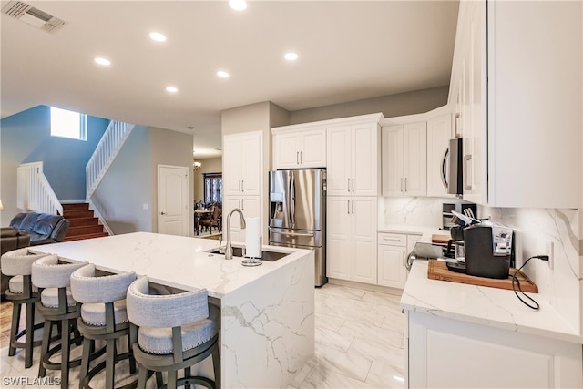 kitchen with white cabinets, tasteful backsplash, a kitchen island with sink, and appliances with stainless steel finishes