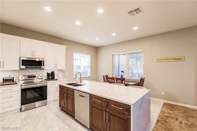 kitchen with stainless steel appliances, light tile floors, light stone countertops, a kitchen island with sink, and sink