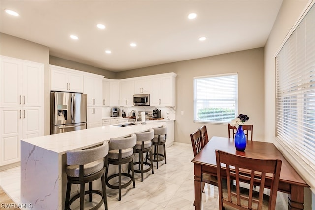 kitchen featuring white cabinetry, stainless steel appliances, light tile floors, light stone counters, and a breakfast bar area