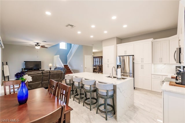 kitchen featuring appliances with stainless steel finishes, white cabinetry, ceiling fan, and an island with sink