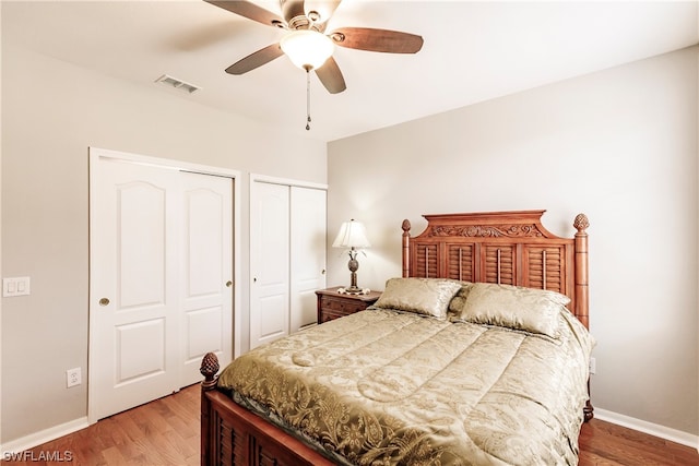 bedroom featuring light hardwood / wood-style floors, ceiling fan, and multiple closets