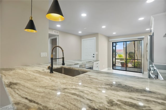 kitchen featuring sink, light stone counters, hanging light fixtures, stainless steel refrigerator, and white cabinetry