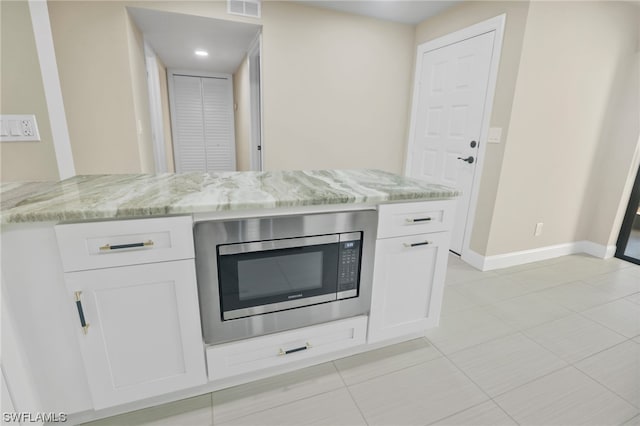 kitchen featuring light tile floors, white cabinets, stainless steel microwave, and light stone countertops