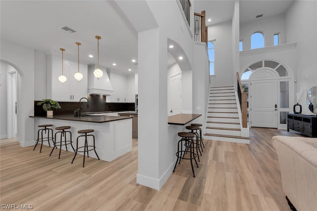 kitchen featuring a breakfast bar, white cabinets, kitchen peninsula, custom exhaust hood, and light hardwood / wood-style flooring