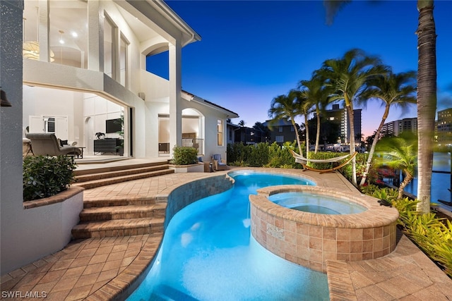 pool at dusk with a patio area and an in ground hot tub