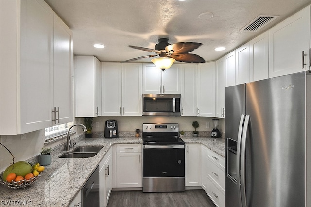 kitchen with dark wood-type flooring, sink, appliances with stainless steel finishes, light stone counters, and white cabinetry