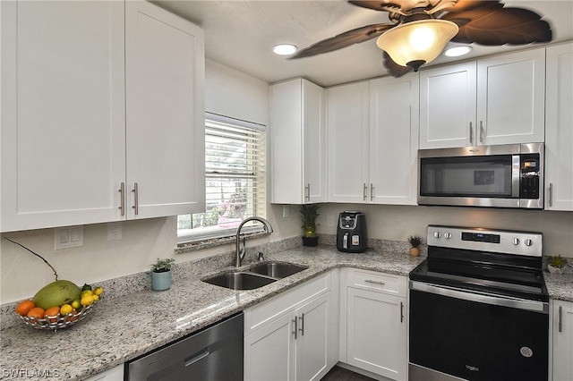 kitchen featuring white cabinets, appliances with stainless steel finishes, light stone counters, and sink