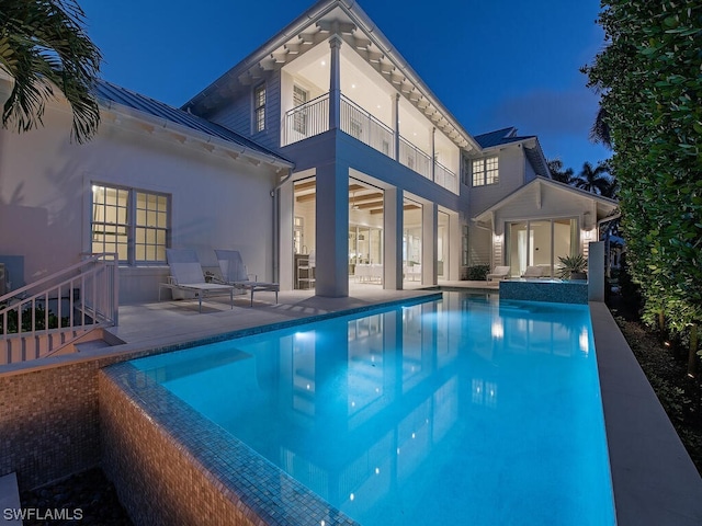 back house at twilight featuring a balcony and a patio area