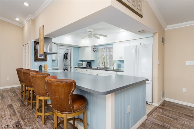 kitchen featuring stacked washing maching and dryer, ceiling fan, white cabinetry, and a breakfast bar