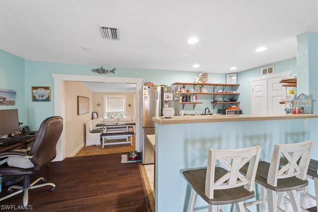 kitchen with stainless steel fridge, kitchen peninsula, a breakfast bar, and dark hardwood / wood-style flooring