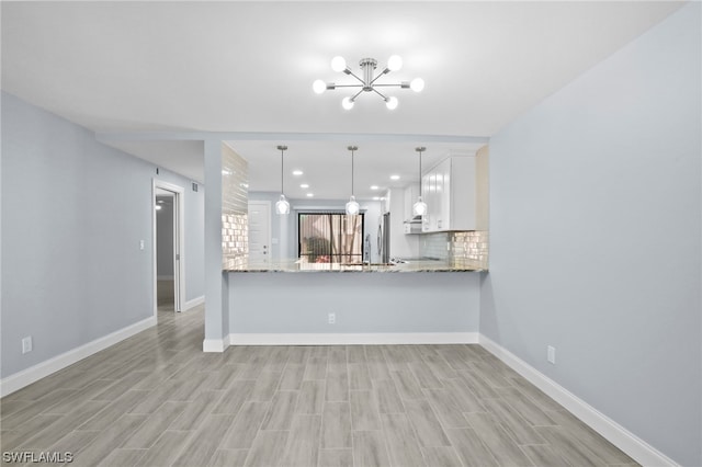 kitchen with a chandelier, pendant lighting, white cabinetry, backsplash, and light stone counters