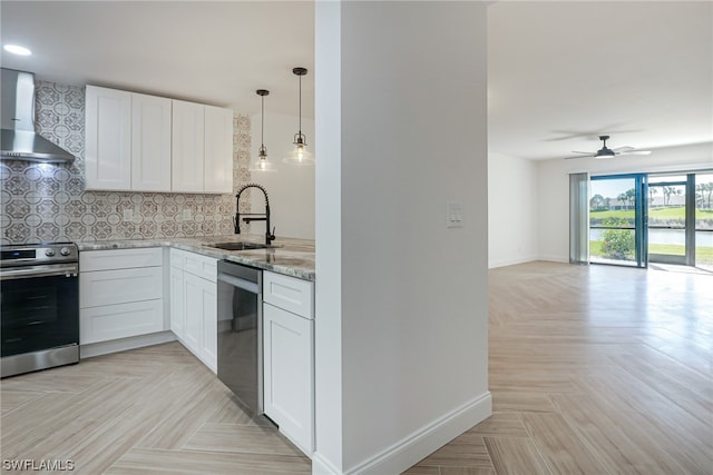 kitchen featuring wall chimney range hood, ceiling fan, appliances with stainless steel finishes, white cabinets, and sink