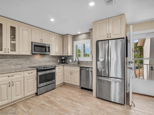 kitchen with sink, light wood-type flooring, stainless steel appliances, light stone counters, and tasteful backsplash